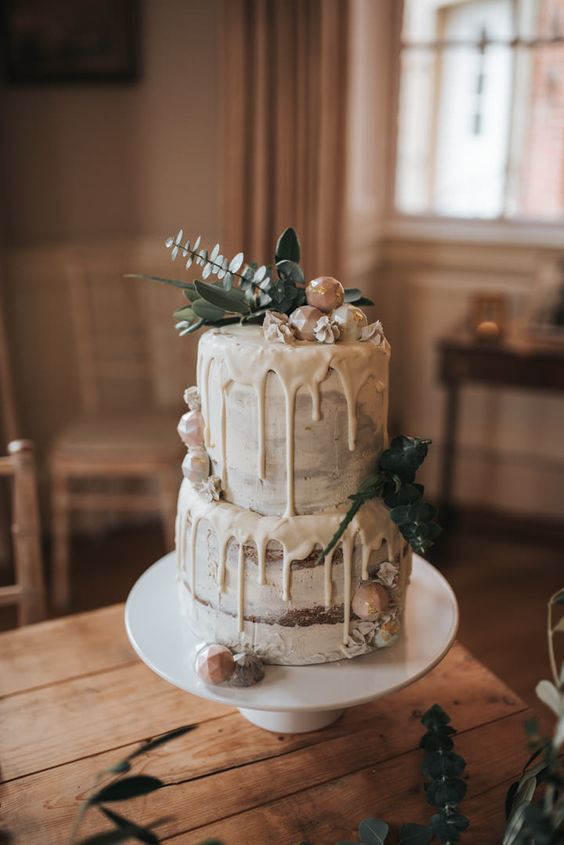 a naked wedding cake with creamy drip, white chocolate, greenery on top for a neutral winter wedding