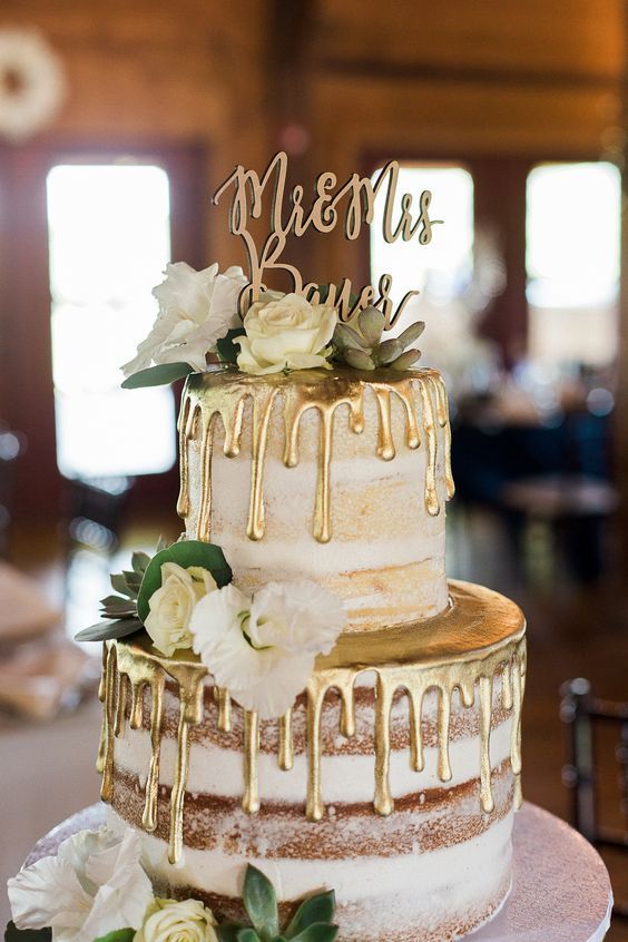 a naked wedding cake with gold drip, white blooms, greenery and a calligraphy topper is a lovely idea