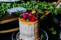 a naked winter wedding cake with caramel drip, bold blooms, fruit and berries is a stylish and cool idea