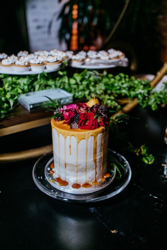 a naked winter wedding cake with caramel drip, bold blooms, fruit and berries is a stylish and cool idea