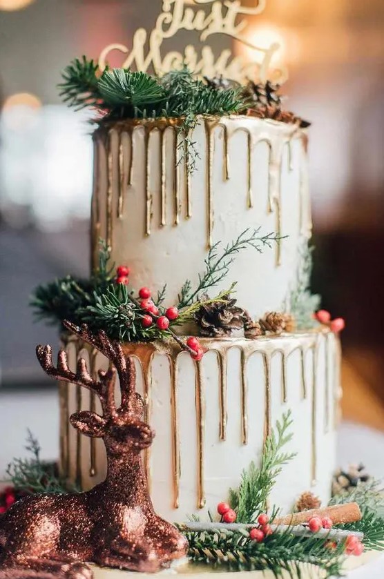 a neutral wedding cake with gold drip, berries, evergreens, pinecones and a gold calligraphy topper is chic