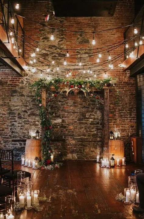 a stained wood Christmas arch decorated with greenery, evergreens, red blooms, antlers, pillar candles with lights over it