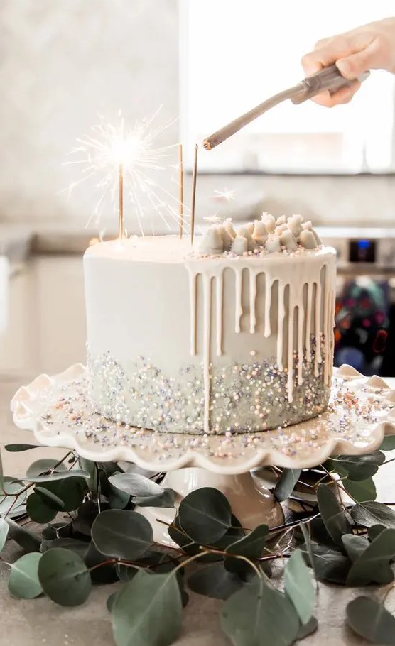 a white wedding cake with beads, glitter and pieces of white chocolate on top plus sparklers is very modern and lovely