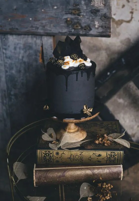 an elegant matte black wedding cake with black drip, cream, chocolate shards and gilded blackberries