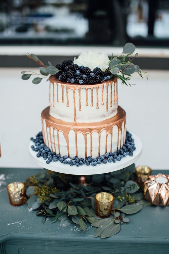 an elegant winter wedding cake with copper drip, fresh berries, greenery and a white bloom on top is a cool and catchy idea