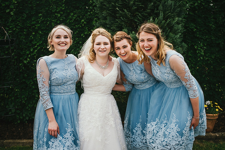 The bride was wearing a lace applique wedding dress with a V neckline and half sleeves, and the bridesmaids were wearing blue gowns with illusion sleeves