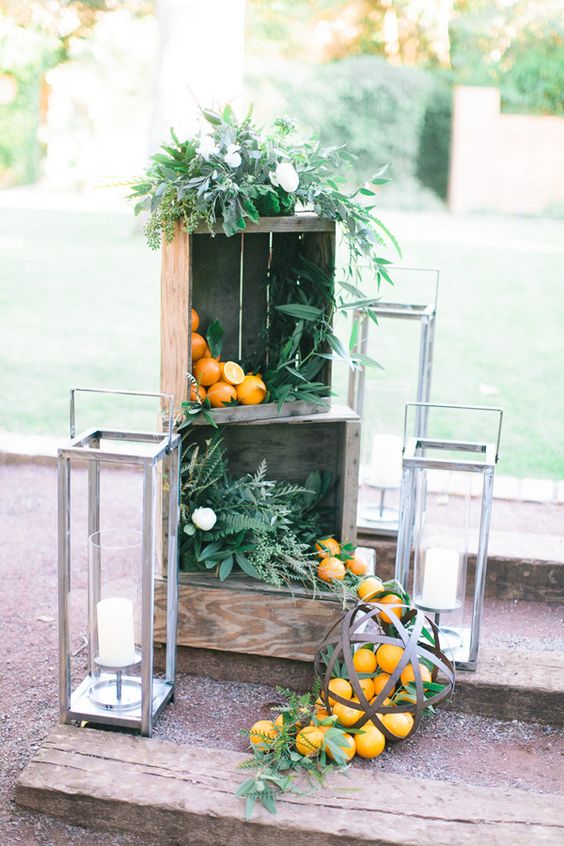 venue decor with crates filled with greenery and iranges, large candle lanterns around