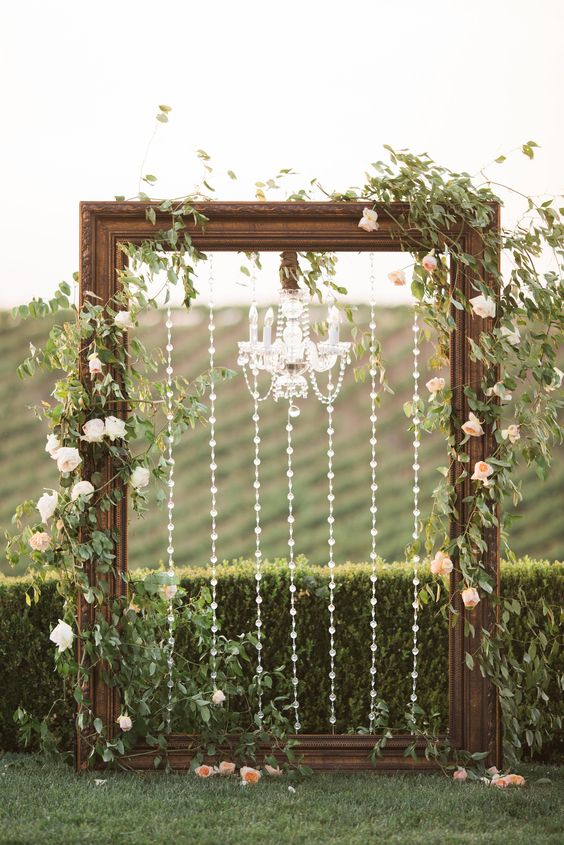 a gorgeous backdrop with a large vintage wooden frame decorated with crystals and a crystal chandelier, greenery and blush blooms