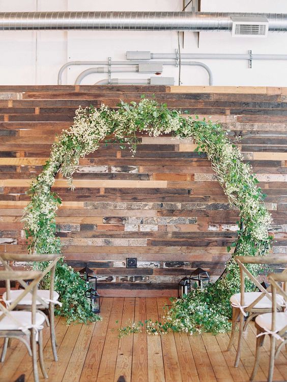 a reclaimed wood wall, candle lanterns and a greenery and bloom weddign arch for an outdoor feeling indoors