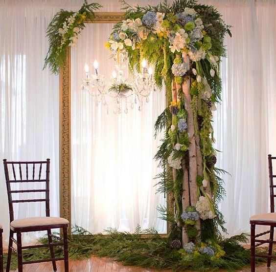 a vintage picture frame with a crystal chandelier, birch branches, pinecones, greenery and blooms for a woodland feel indoors