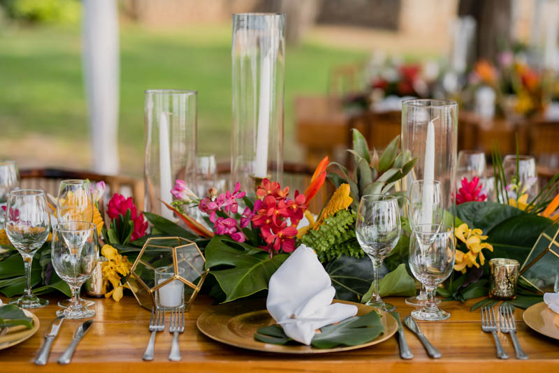 The tables were decorated with runners of tropical leaves and colorful flowers, geometric candle holders