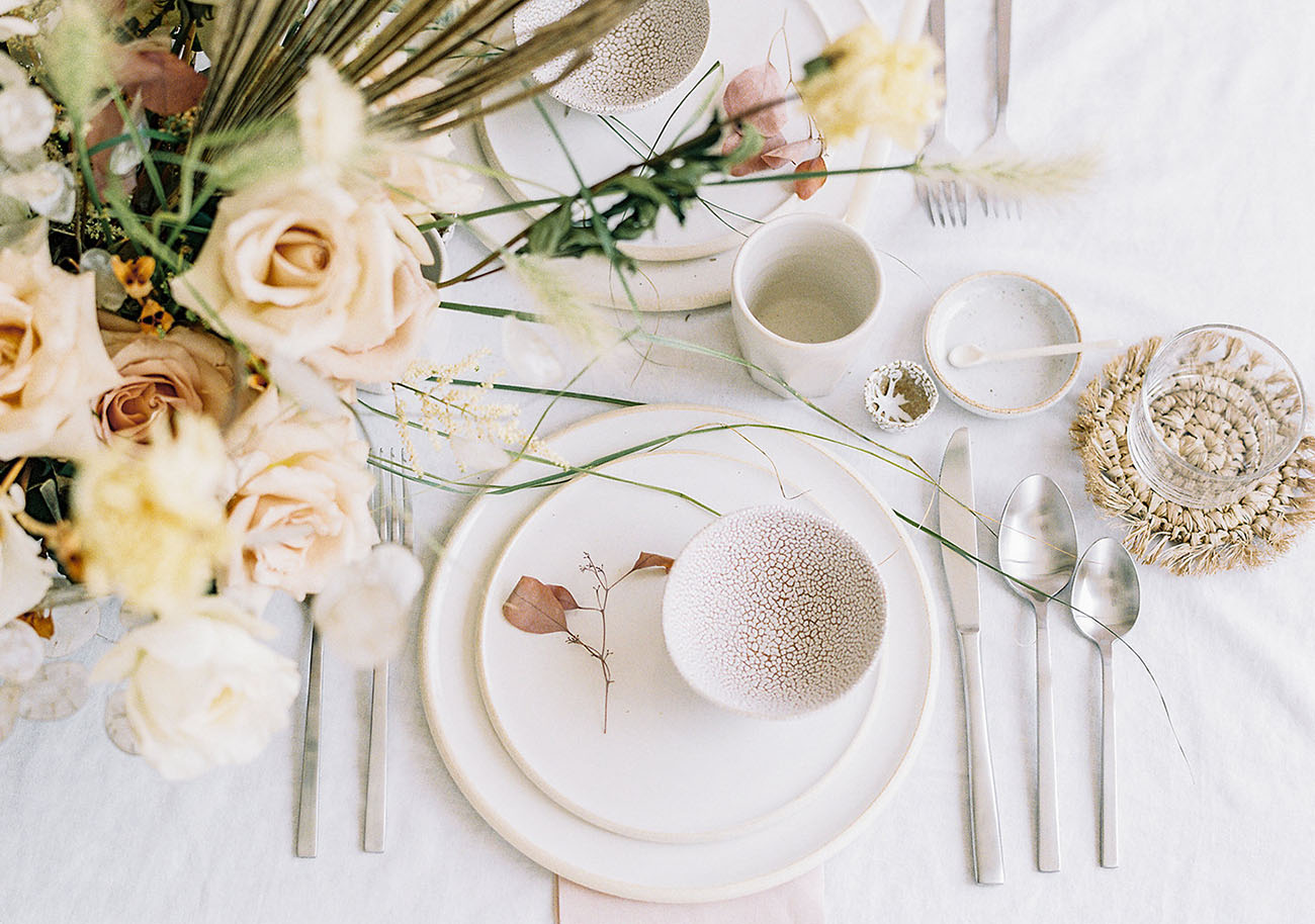 The tablescape features unique pottery and blush and neutral blooms