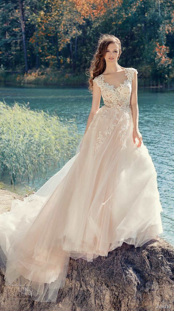 a blush cap sleeve wedding dress with a lace applique bodice and a full layered skirt