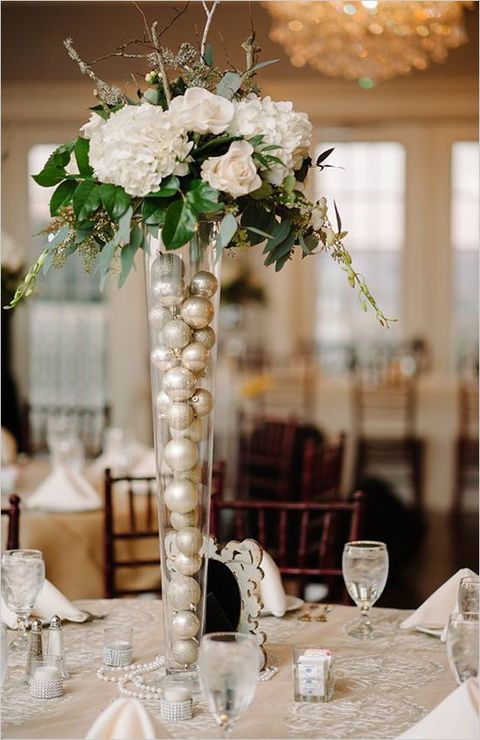 an elegant centerpiece with white blooms and greenery and silver ornments inside the vase