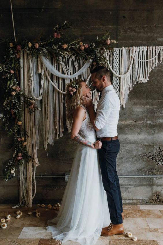 a macrame wedding backdrop with greenery and blush blooms for a boho wedding