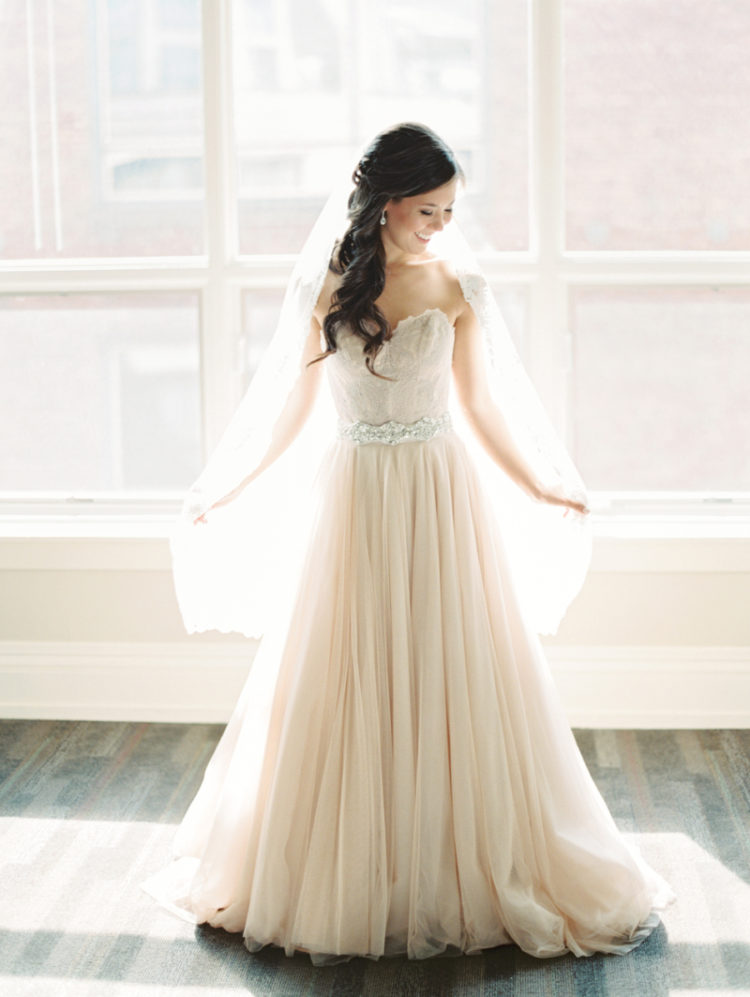 a strapless blush wedding dress with a lace embroidered bodice, an embellished belt and a matching veil