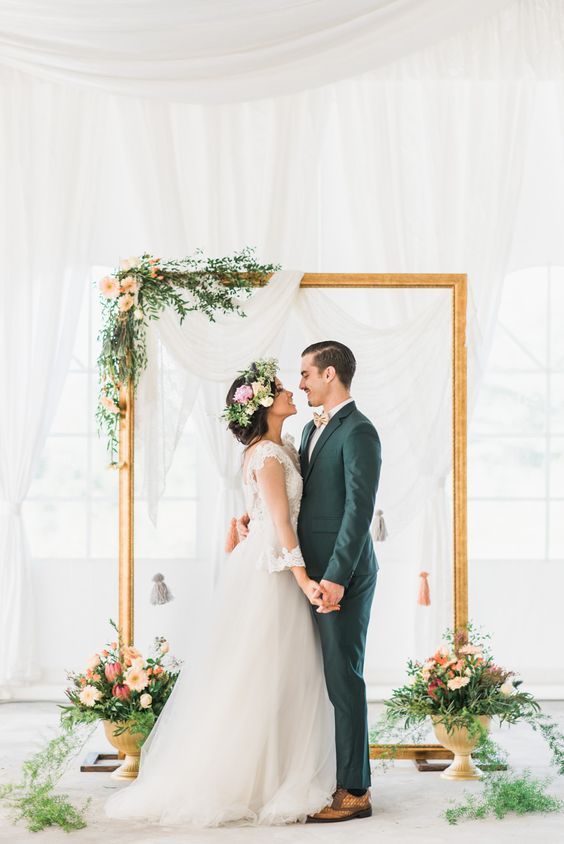 an ethereal draped fabric backdrop, an oversized picture frame decorated with greenery and blooms