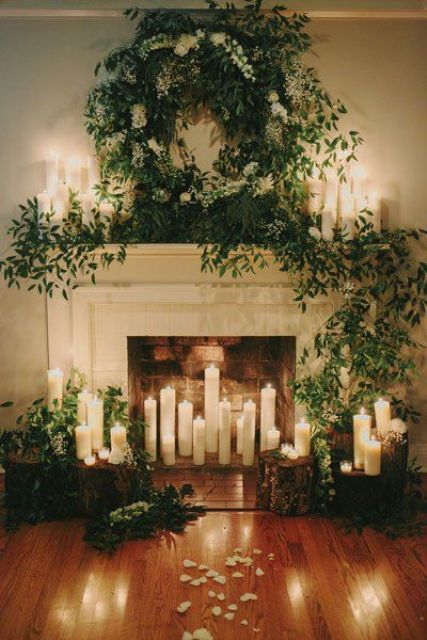 a fireplace covered with lush greenery,, lots of candles and tree stumps