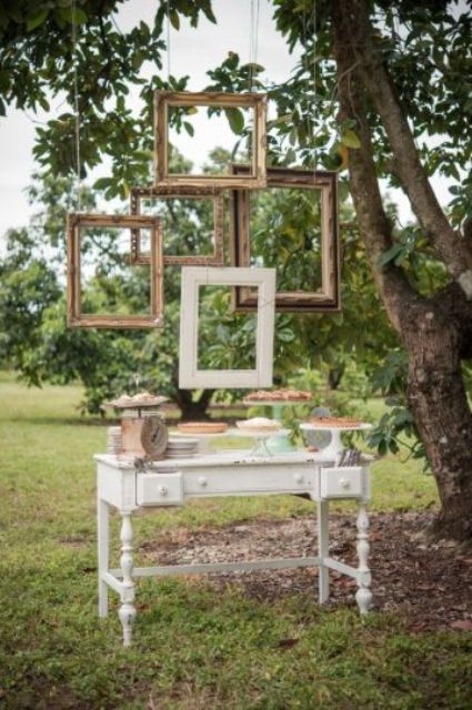 an outdoor dessert station with picture frames hanging over it as a backdrop