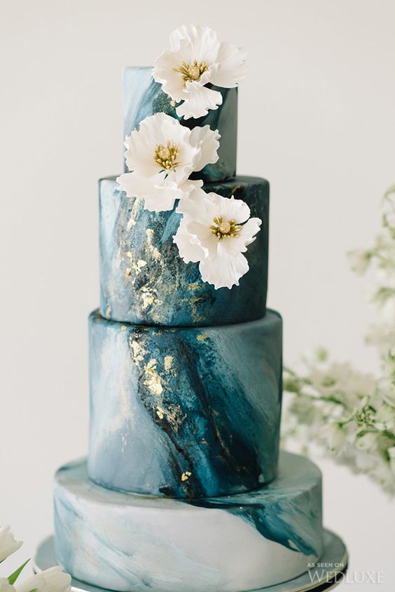 a blue marble wedding cake is topped with gilded flowers that pick up on the subtle gold flecks