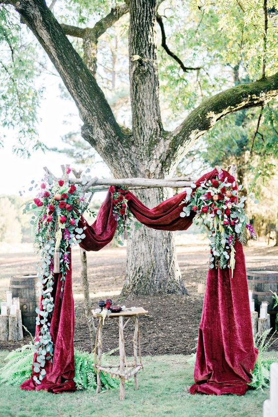 a burgundy velvet drapery and lush burgundy roses and greenery for the arch decor