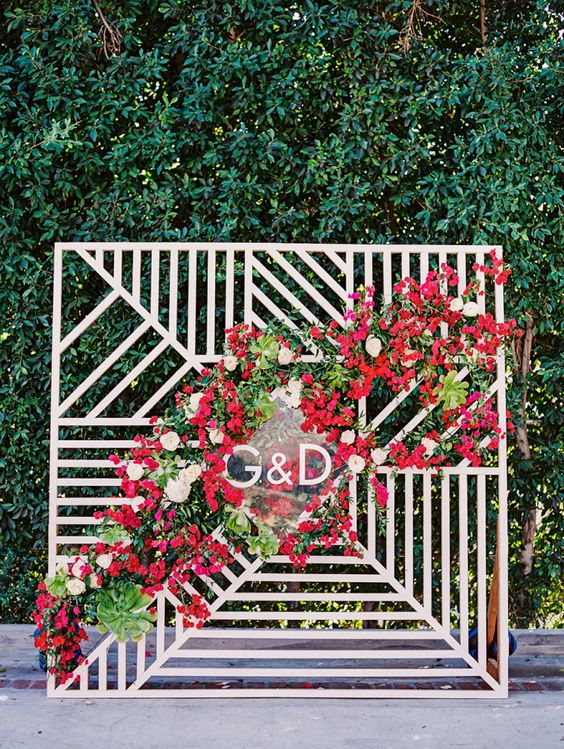 a modern geometric backdrop with a lush red flower cascading garland and monograms