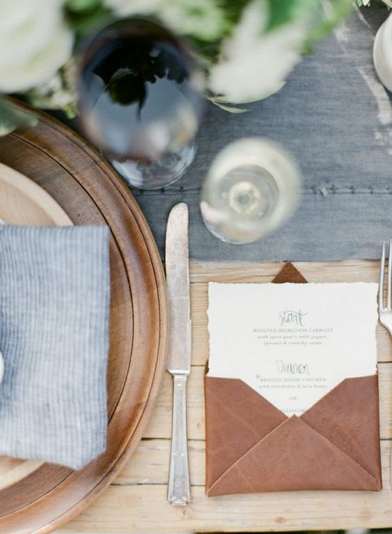 a leather wedding menu card envelope matches a wooden charger and adds texture to the table