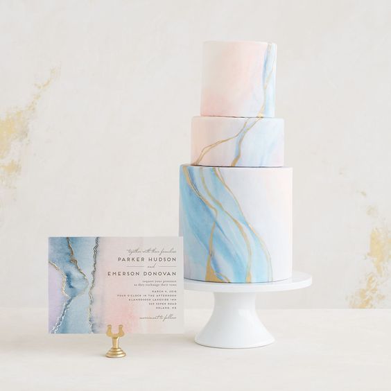 a romantic light blue and pink marbleized wedding cake with gold leaf and a matching card