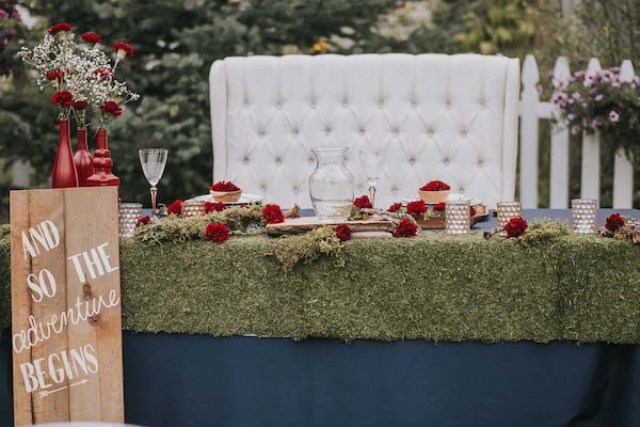 The wedding tables were covered with moss, with red blooms, baby's breath and wooden touches to give it a rustic feel