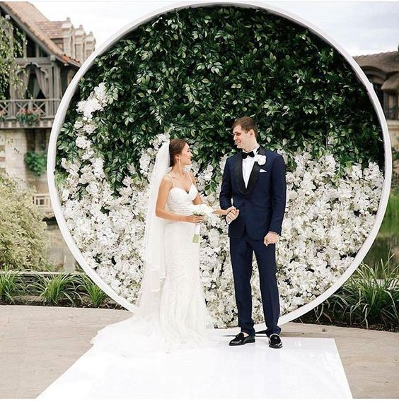 a circular backdrop adorned with greenery and white blooms which will set a modern and elegant wedding statement