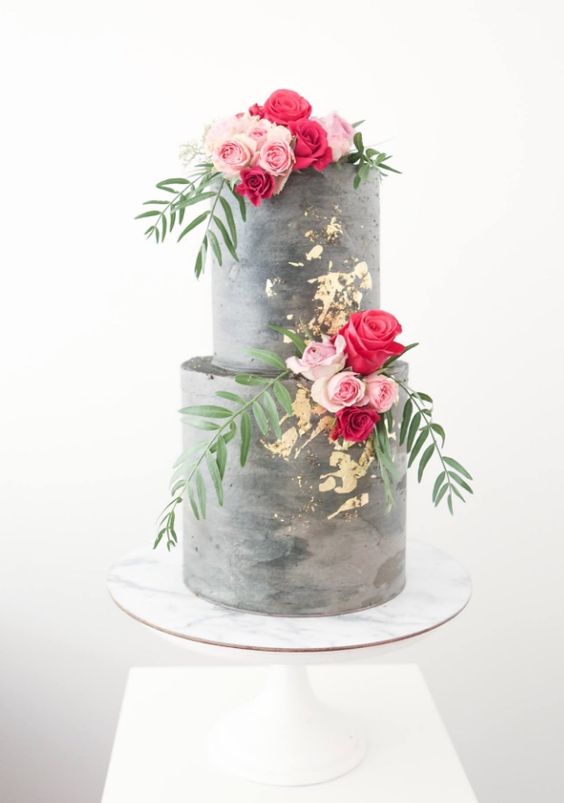 a concrete wedding cake with gold leaf and bold blooms and greenery looks very modern