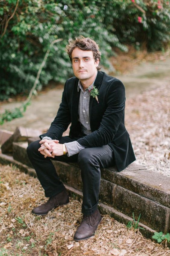 a relaxed groom's look with a grey shirt, black pants, brown boots and a black velvet jacket
