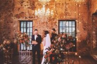13 the cermeony space decorated with glam chandeleirs, lights and lush florals on stands