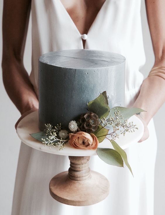 a concrete-inspired round wedding cake with blooms and foliage looks romantic and modern