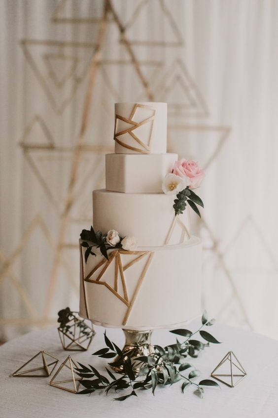 a white wedding cake with geometric layers and gold geometric details