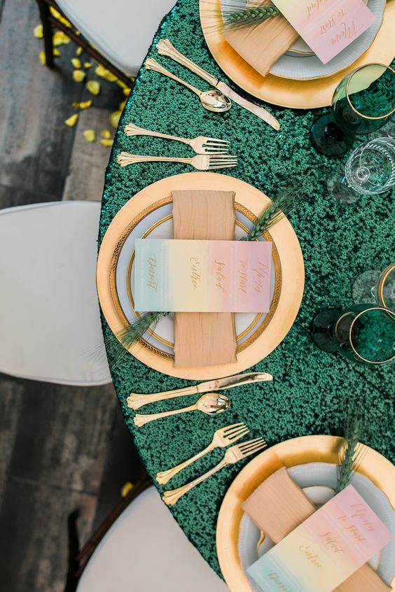 an emerald sequin tablecloth, gold cutlery and chargers, emerald and gold rim glasses for a chic table setting