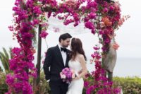 20 a lush and bold fuchsia bloom wedding arch and a backdrop of the sea behind
