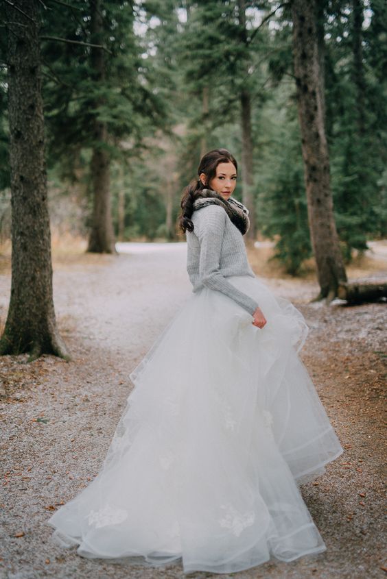 a grey comfy sweater over a princess-style wedding dress and a faux fur scarf looks very contrasting