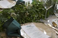 21 emerald napkins and candleholders, gold cutlery and a lush greenery garland in the center
