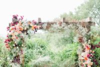 23 a rustic wooden arch with lush floral decor on both sides and tree stumps for a rustic feel