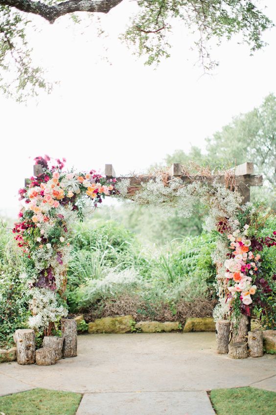 a rustic wooden arch with lush floral decor on both sides and tree stumps for a rustic feel