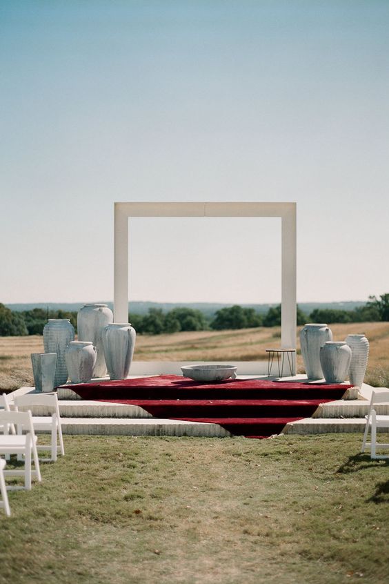 a natural backdrop with a minimalist white arch and vases around the arch
