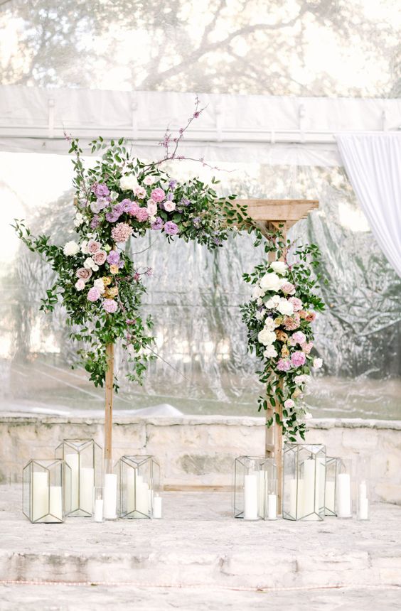 a wooden arch with asymmetric decor of lilac and white blooms and candle lanterns around