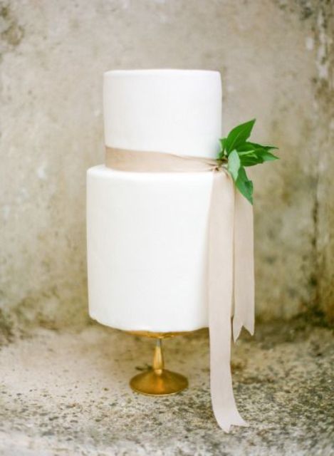 a white wedding cake with a blush ribbon and foliage for a cute and chic look