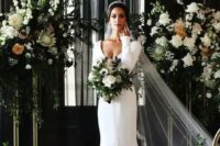 a beautiful mermaid plain wedding dress with a deep neckline and long sleeves plus a train and a cathedral veil for a luxurious wedding