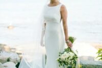 a lovely modern mermaid sleeveless wedding dress with an empire waist and a high neckline plus a cathedral veil for a tropical bride