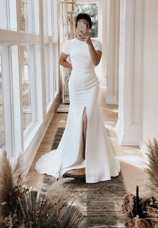 an ultra-modern plain fitting wedding dress with a high neckline, short sleeves, a front slit and a train for a minimalist bride