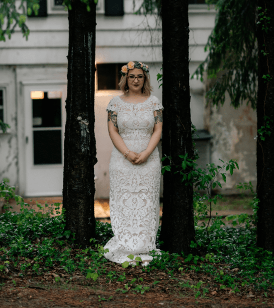 The bride was wearing a cream sheer lace wedding dress with short sleeves and a bateau neckline that showed off her tattoos
