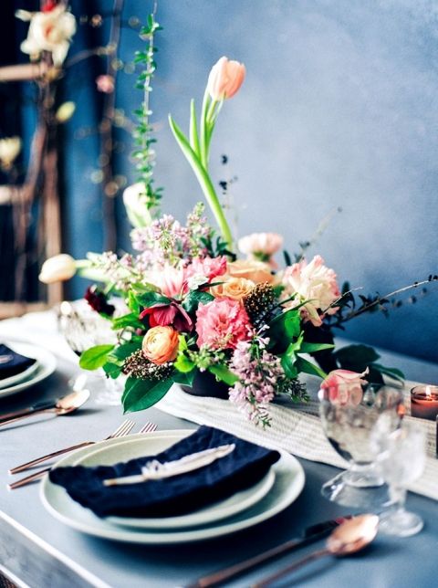 a moody spring table setting with a bold floral centerpiece, a navy napkin and a feather