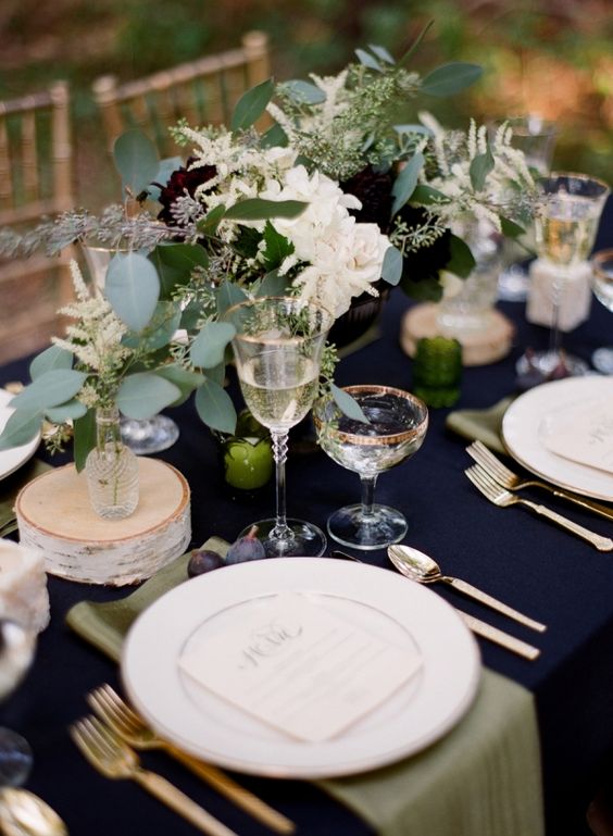 a navy tablecloth and gold cutlery create an elegant look, and lush greenery and blooms add a messy casual feel